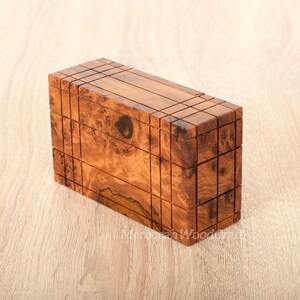 May include: A rectangular wooden box featuring a natural brown burl grain pattern with dark knots and a grid of thin, incised vertical and horizontal lines across the exterior surfaces. The box has a smooth finish and a visible wood grain texture.