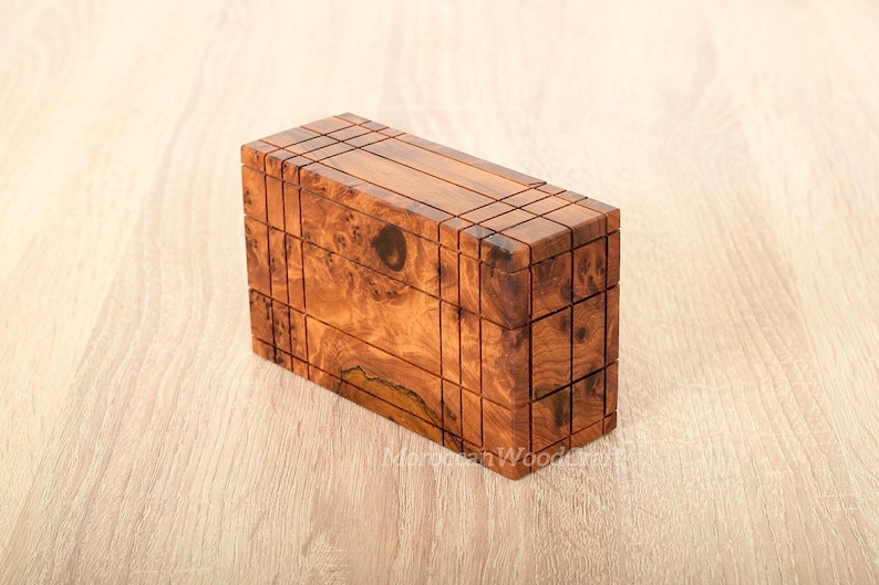 May include: A rectangular wooden box featuring a natural brown burl grain pattern with dark knots and a grid of thin, incised vertical and horizontal lines across the exterior surfaces. The box has a smooth finish and a visible wood grain texture.