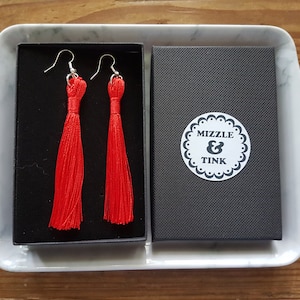 May include: A pair of red tassel earrings in a black box with a white label that says "Mizzle & Tink".