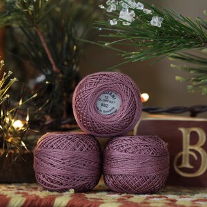 May include: Three spools of mauve embroidery floss, each with a white label that reads "DMC 12 GLORYAST 882 Made in Romania".