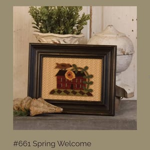 May include: A framed artwork with a rustic aesthetic. The image features a red house with a sunflower and green foliage, set against a beige background. The frame is dark brown. The text at the bottom reads "#661 Spring Welcome."