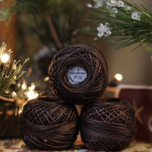 May include: Three spools of brown embroidery floss, stacked on top of each other. The top spool has a white label that reads "Colorfast P 12".