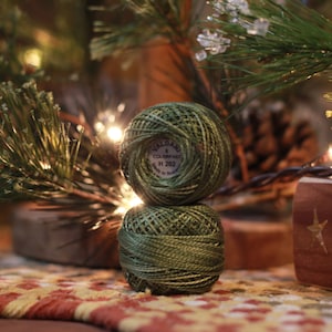 May include: Two spools of green embroidery floss stacked on top of each other. The top spool has a label that reads "Valdani 8 Colors Ass H 202".