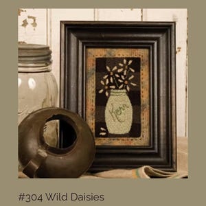 May include: Framed artwork featuring a jar of daisies. The artwork is in a black frame and has a black and brown checkered background. The jar is light green with the word "Kern" on it. The image also includes a glass jar and a metal lid.