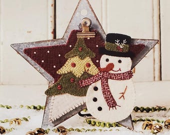 May include: A star-shaped Christmas ornament with a snowman and tree design. The ornament is made of felt and metal, with a clip for hanging. The snowman has a black hat, red scarf, and button eyes. The text "SNOW JOYFUL STAR" is visible. Size: 4.5" x 5.5".