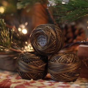 May include: Three spools of brown and gold embroidery floss with a label that reads "Valdani 8 Colorfast P9".