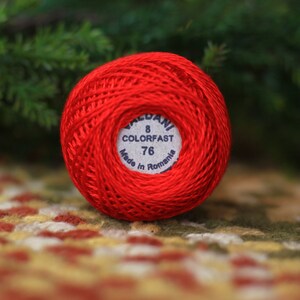 May include: A ball of red embroidery floss with a white label that reads "Valdani 8 Colorfast 76 Made in Romania".