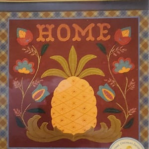 May include: A decorative wall hanging or pillow kit featuring a pineapple design with the word "HOME". The design includes floral accents and the text "Welcome Home". Finished size is 16 x 16 inches.