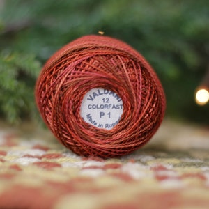 May include: A spool of red and brown embroidery floss with a white label that reads "Valdani 12 Colorfast P 1 Made in Rome".