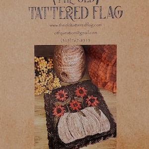 May include: A rustic image featuring a primitive punch needle pattern titled "Old White Pumpkin." The design includes a white pumpkin and red flowers on a dark background. The finished size is 8 inches square.