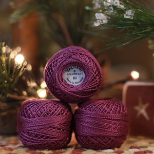 May include: Three spools of purple embroidery floss, each with a white label that reads "Valdani Colorfast 82 Made in Romania".