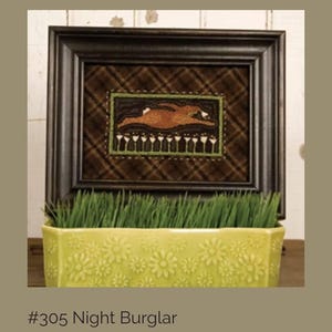 May include: Framed artwork featuring a brown rabbit with white accents, framed in a dark brown frame. The background is a brown plaid pattern. The artwork is displayed above a yellow floral planter filled with green grass. The text "#305 Night Burglar" is at the bottom.