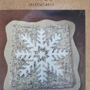 May include: A primitive punch needle pattern with a white snowflake design on a square, measuring 6.5 inches. The text "THE OLD TATTERED FLAG" is at the top. The text "No Two Alike" is also visible.