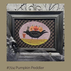 May include: Framed artwork featuring a black crow carrying a small orange bucket, with three carved pumpkins on its back. The crow stands on a yellow field within a pink oval, set against a brown patterned background. The frame is dark gray.