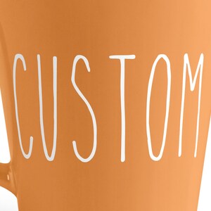 Pu&ograve; includere: Tazza in ceramica arancione con la scritta "CUSTOM" in bianco sul davanti.