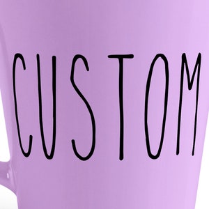 Pu&ograve; includere: Una tazza in ceramica lavanda con la parola "CUSTOM" scritta in nero sul davanti.