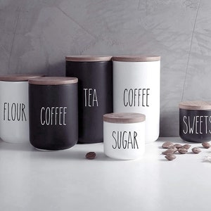 May include: Set of six black and white ceramic canisters with wooden lids. The canisters are labeled "Flour", "Coffee", "Tea", "Coffee", "Sugar", and "Sweets".