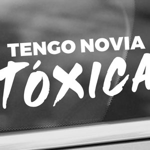 K&ouml;nnte beinhalten: Wei&szlig;er Vinyl-Aufkleber mit dem Text "TENGO NOVIA T&Oacute;XICA" in einer fetten, stilisierten Schrift.