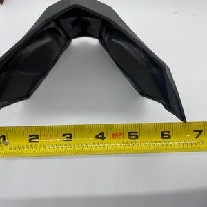 Puede incluir: Un objeto de pl&aacute;stico negro con forma curva, medido con una cinta m&eacute;trica amarilla. La cinta m&eacute;trica muestra una medida de 12,7 cm.