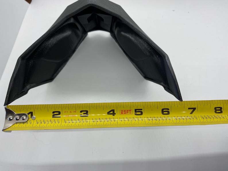 Puede incluir: Un objeto de pl&aacute;stico negro con forma curva, medido con una cinta m&eacute;trica amarilla. La cinta m&eacute;trica muestra una medida de 12,7 cm.