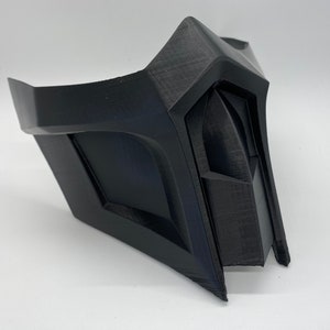 Puede incluir: Una m&aacute;scara de pl&aacute;stico negro con un dise&ntilde;o geom&eacute;trico. La m&aacute;scara tiene una forma afilada y angular y recuerda a un personaje de un videojuego o pel&iacute;cula.