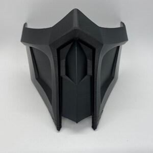 Puede incluir: Una m&aacute;scara de pl&aacute;stico negro con un dise&ntilde;o afilado y angular. La m&aacute;scara tiene un patr&oacute;n en forma de diamante en relieve en el centro.