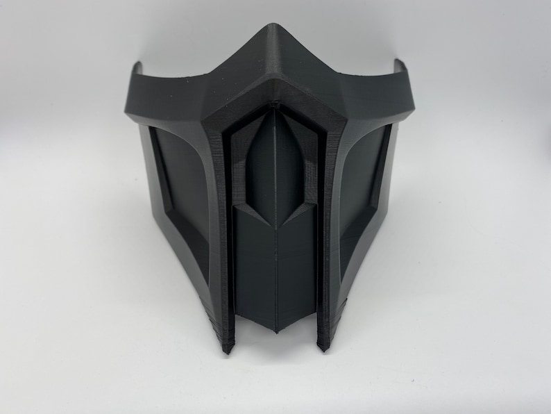 Puede incluir: Una m&aacute;scara de pl&aacute;stico negro con un dise&ntilde;o afilado y angular. La m&aacute;scara tiene un patr&oacute;n en forma de diamante en relieve en el centro.