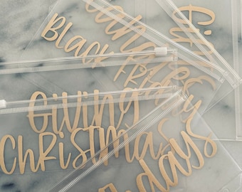 May include: Clear plastic zippered pouches with gold lettering. The pouches are labeled "Black Friday", "Giving", "Christmas", "Birthdays", and "Camp".