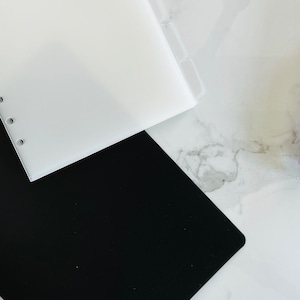 May include: A white plastic binder with clear dividers and a black plastic binder.