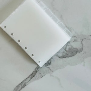 May include: A white plastic page divider with six tabs for a disc bound planner.