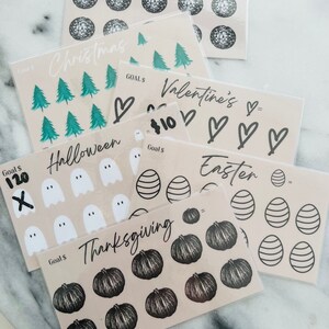 May include: A set of ten printable goal tracker sheets featuring various holiday themes. Each sheet includes a goal amount, a title, and a grid of icons to color in as goals are achieved. The themes include New Years, Christmas, Valentine's Day, Easter, Halloween, and Thanksgiving.
