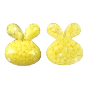 May include: Two yellow resin bunny shaped charms with a speckled texture.