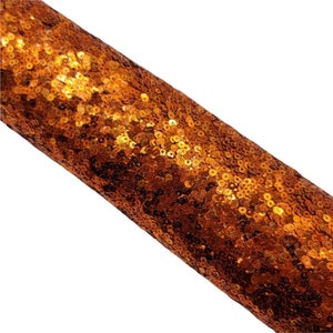 May include: A roll of orange sequin fabric. The sequins are small and round, and they are densely packed together. The fabric has a shiny, metallic finish.