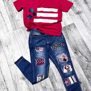 May include: A red t-shirt with a white and blue American flag design and a pair of blue jeans with multiple patches in red, white, and blue.