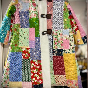 May include: A patchwork coat with a hood, featuring a variety of floral and patterned fabrics in shades of blue, green, pink, and red. The coat has a white faux fur lining and toggle closures. The text "Happens in the" is visible on the hanger.