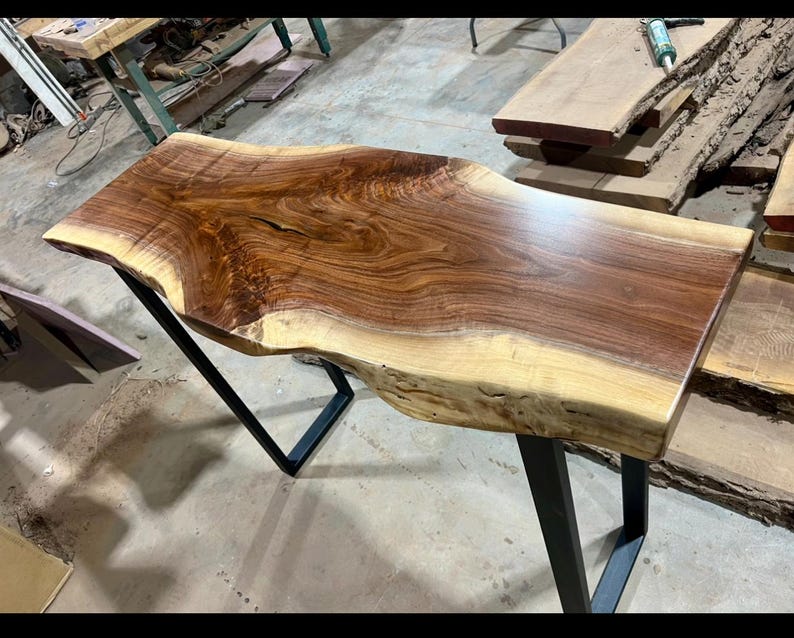 Bring the warmth of the Ozarks into your home with this stunning, handcrafted live-edge black walnut console table. Featuring an exceptionally unique, swirling grain pattern and the beautiful natural contrast between dark heartwood and creamy sapwood, this piece serves as a timeless functional art piece for any entryway, hallway, or behind-the-sofa display. Paired with sleek, modern industrial metal legs, it perfectly balances rustic charm with contemporary design.