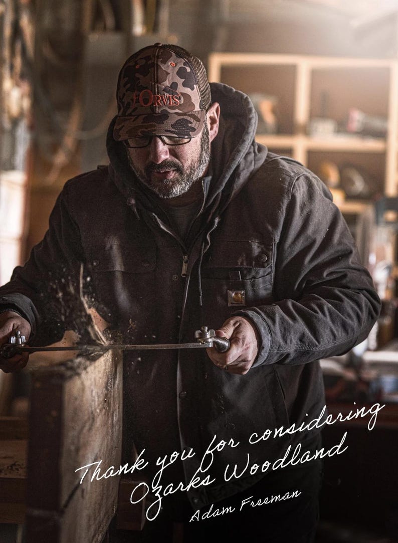 May include: A man wearing a camouflage cap and glasses, using a saw on a wooden plank. He is wearing a dark jacket. The image includes the text "Thank you for considering Ozarks Woodland" and the name "Adam Freeman".