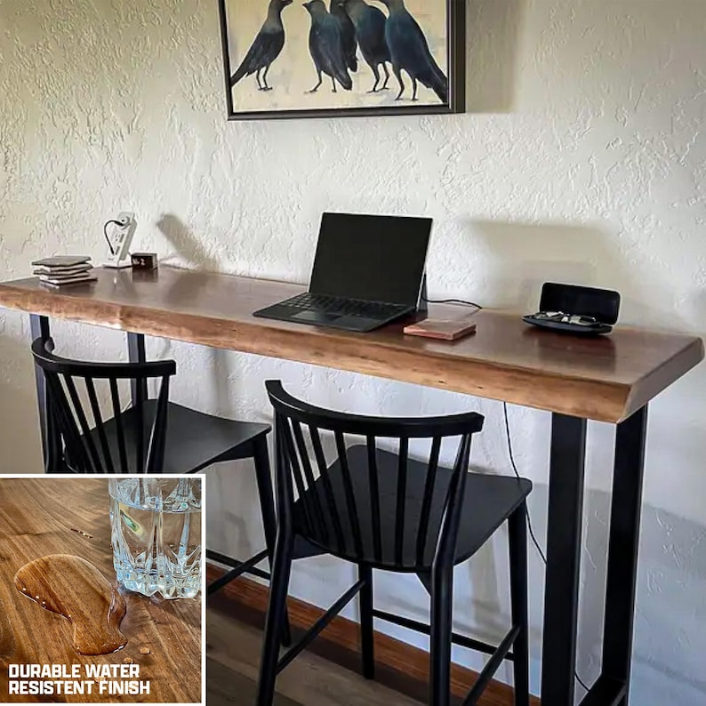 May include: A live edge wooden bar table with black metal legs, two black chairs, and a laptop. The table has a durable water-resistant finish. A painting of crows hangs above the table.