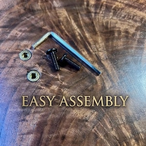 May include: Close-up of a wooden surface with the text "EASY ASSEMBLY" in gold lettering. Two black screws, a silver Allen key, and two gold-coloured screw holes are visible.