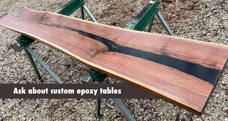 Handcrafted American black walnut live-edge table top featuring a smooth black epoxy resin river inlay. This premium, artisanal wood slab showcases deep chocolate grain patterns and natural live edges, perfect for a modern farmhouse console table or custom dining piece. Milled and finished in the Ozark Mountains