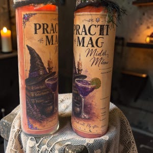 May include: Two tall cylindrical candles with orange wax, each wrapped in a beige label featuring the text "PRACTICAL MAGIC" and "Midnite Mimosas". The labels display illustrations of a witch hat, stacked books, a cauldron, and a purple cocktail.