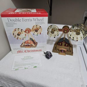 May include: A Mr. Christmas Double Ferris Wheel set including a motorized double ferris wheel model, a power cord, an instruction manual, and the original cardboard box featuring product imagery and text labels.
