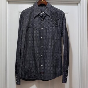 May include: A dark gray long-sleeve button-down shirt with a textured pattern. The shirt features embroidered floral designs on the chest and lower left side. It has a classic collar and buttoned cuffs, displayed on a wooden hanger.