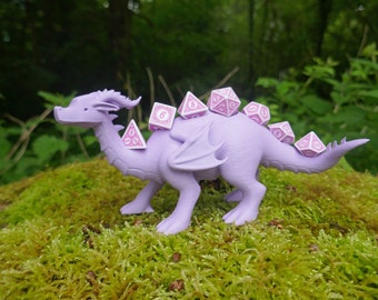 May include: A purple plastic dragon figurine with a white and pink design. The dragon is carrying six pink and white dice on its back.