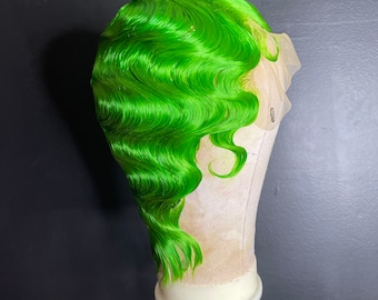 Puede incluir: Una peluca verde brillante con un estilo ondulado, mostrada en un soporte para pelucas.