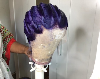 Puede incluir: Una peluca morada con un estilo ondulado, colocada en un soporte para pelucas.