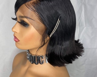 May include: A black bob wig with a lace front and a middle part. The wig is styled with a side part and has a slight wave. The wig is on a mannequin head with a silver choker necklace.
