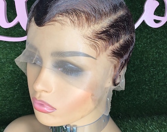 Puede incluir: Una peluca corta de color marrón oscuro con un frente de encaje y un estilo ondulado. La peluca está en una cabeza de maniquí con un collar gargantilla transparente que dice "OUCH".