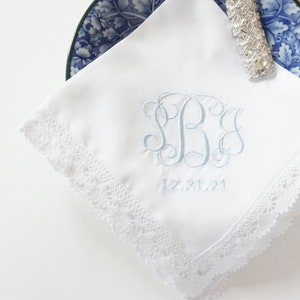 May include: White handkerchief with a blue embroidered monogram and the date 12.31.21. The handkerchief has a white lace trim.