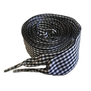 May include: A coiled pair of black and white gingham shoelaces. The laces are made of a woven material with a traditional chequered design. The ends are finished with aglets.